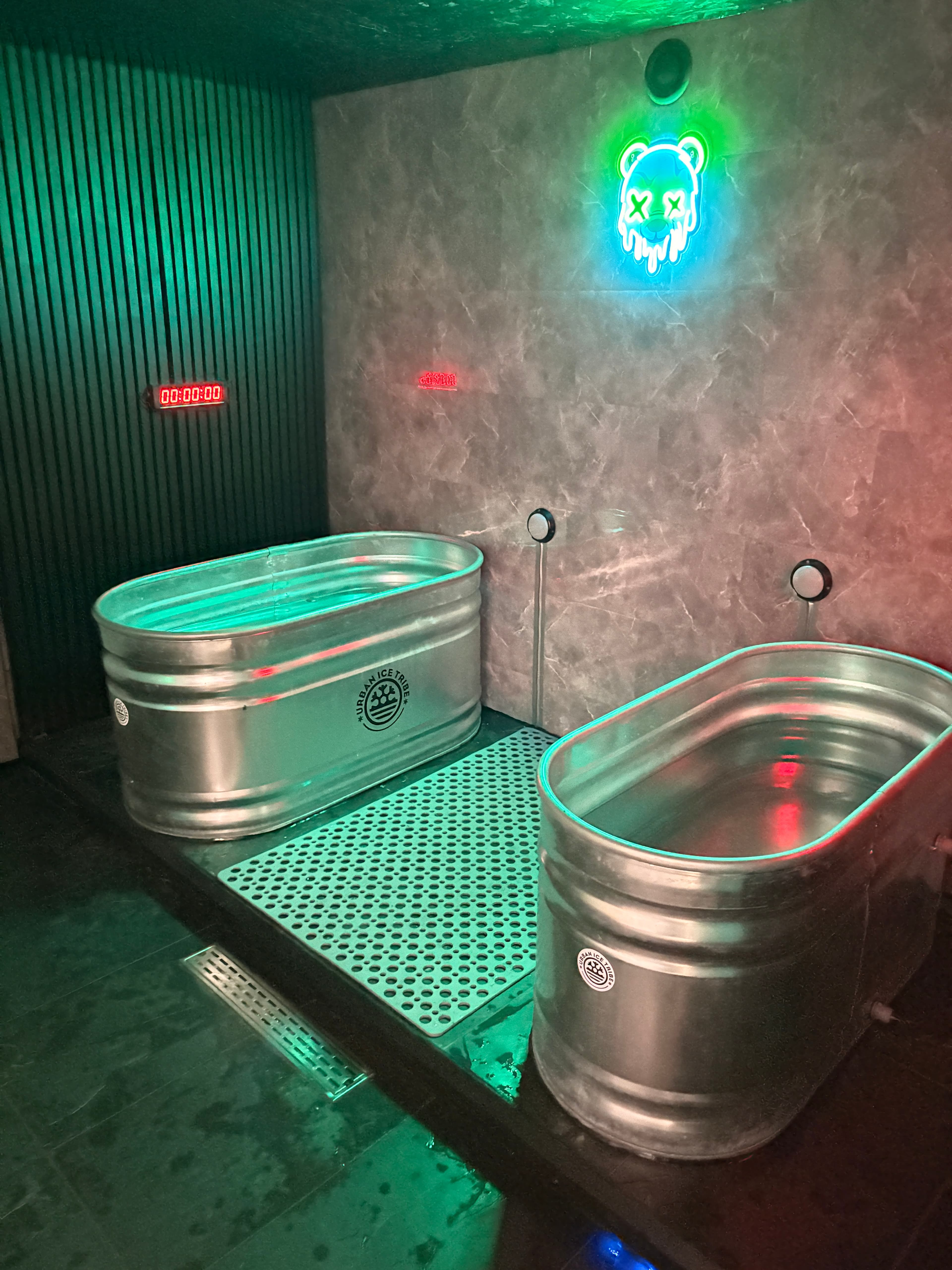 Two galvanized metal ice baths in a room with green and red neon accents.