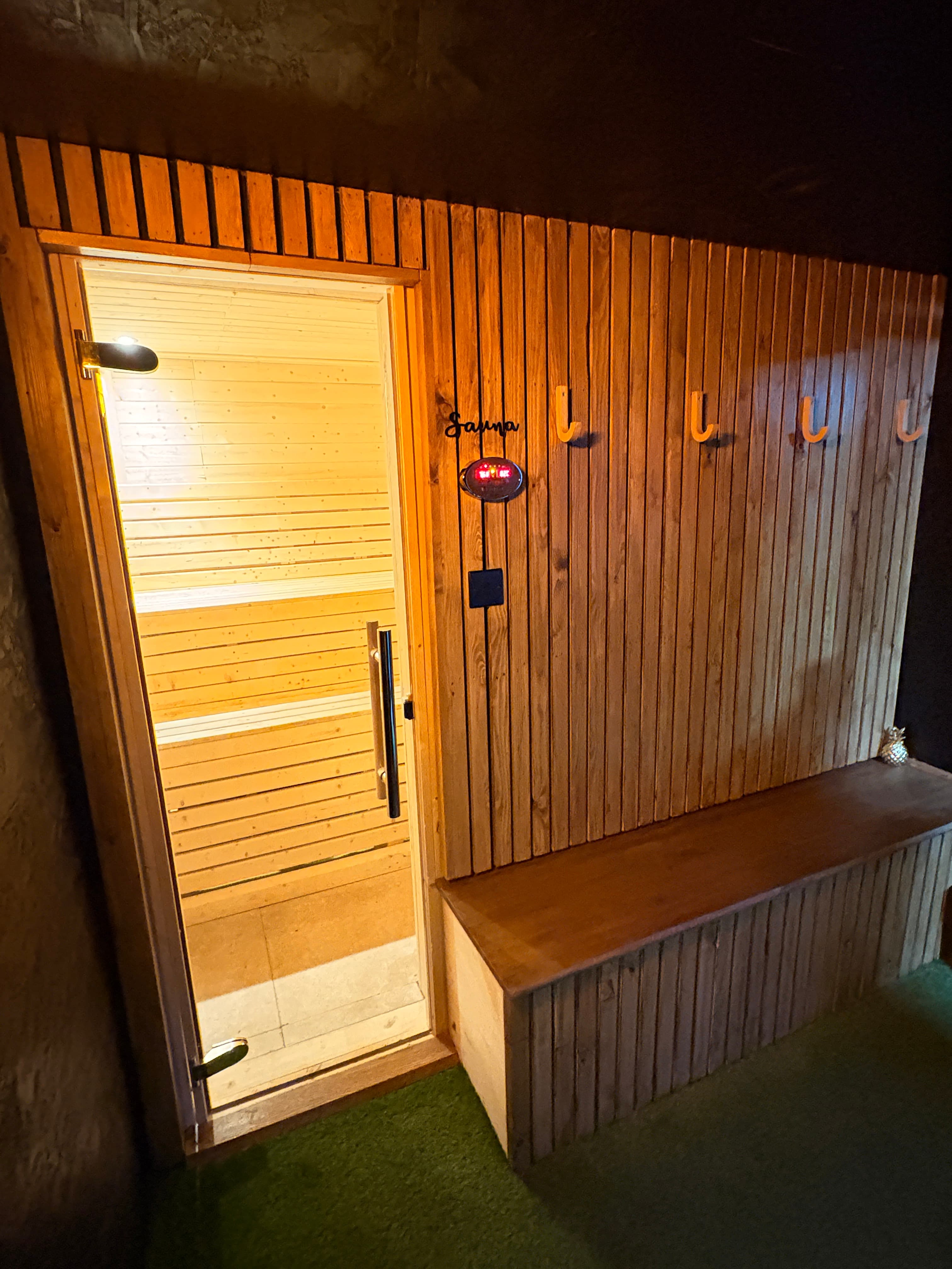 Wooden outdoor sauna at night featuring a glass door and warm interior lighting.