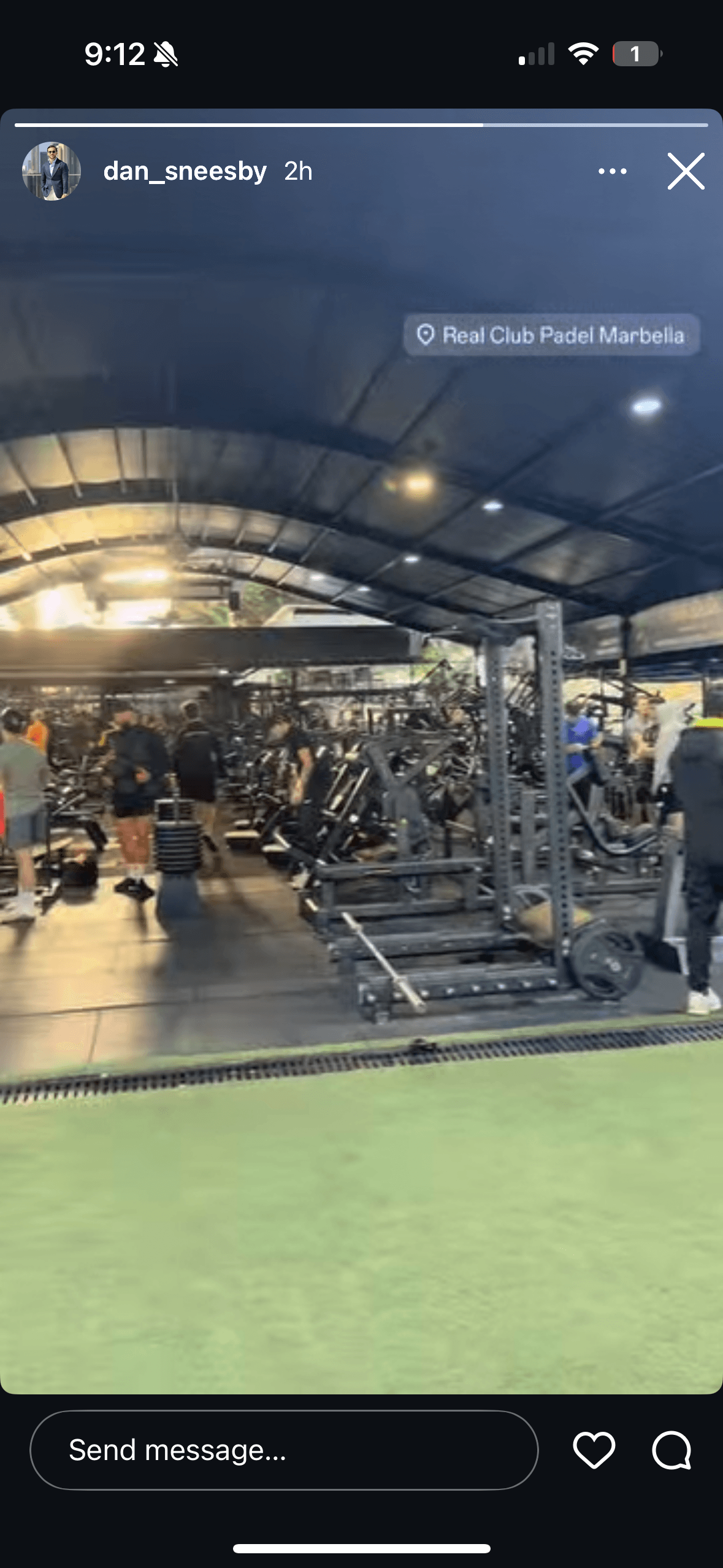 People exercising in a large indoor gym with weightlifting equipment and a green turf area.